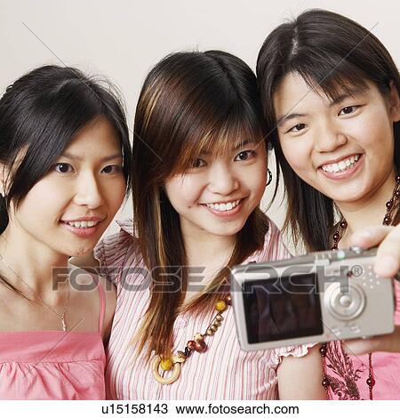 Stock Image - Close-up of three young women taking a picture of themselves. Fotosearch