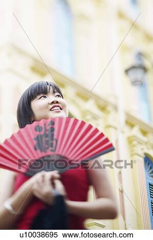 Low angle view of a young woman holding a folding fan View Large Photo Image Stock Photography - Low angle view of a young woman holding a folding fan. Fotosearch
