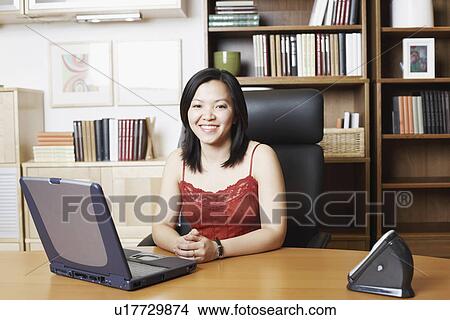 Picture - Portrait of a businesswoman sitting in front of a laptop smiling. Fotosearch