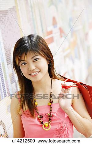 Stock Photo - Portrait of a young woman carrying a shopping bag and smiling. Fotosearch