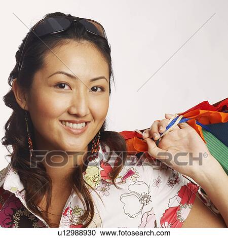 Stock Image - Portrait of a young woman carrying shopping bags and smiling. Fotosearch