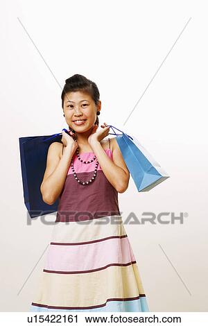 Stock Image - Portrait of a young woman carrying shopping bags and smiling. Fotosearch