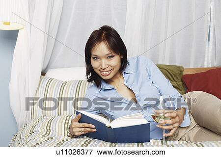Portrait of a young woman holding a wineglass and a book on the bed View Large Photo Image Stock Photo - Portrait of a young woman holding a wineglass and a book on the bed. Fotosearch