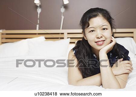 Portrait of a young woman lying on the bed thinking with her hand on her chin View Large Photo Image Stock Photo - Portrait of a young woman lying on the bed thinking with her hand on her chin. Fotosearch