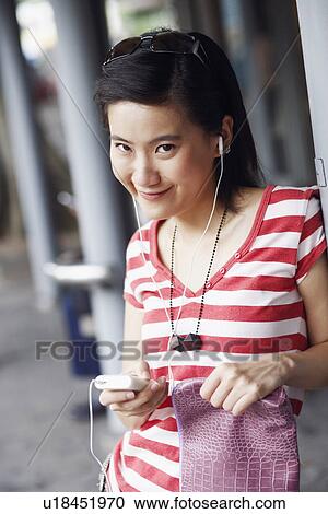 Stock Image - Portrait of a young woman smiling and listening to music. Fotosearch
