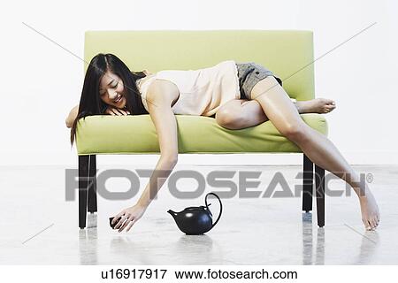 Stock Photo - Side profile of a young woman lying on a couch holding a tea cup. Fotosearch