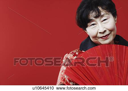 Stock Image - Portrait of a mature woman holding a folding fan. Fotosearch