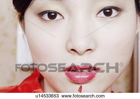 Portrait of a young woman applying lip gloss View Large Photo Image Stock Image - Portrait of a young woman applying lip gloss. Fotosearch