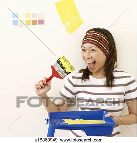 Stock Photo - Close-up of a young woman sticking her tongue out and holding a paintbrush. Fotosearch