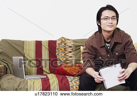 Stock Image - Portrait of a mid adult man sitting on a couch and holding a diary. Fotosearch