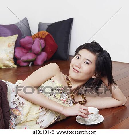 Stock Photo - Portrait of a young woman lying on the floor and holding a cup of tea. Fotosearch
