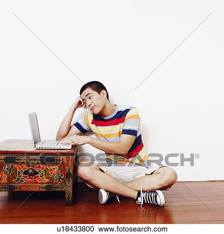 Stock Image - Young man sitting on the floor and using a laptop. Fotosearch