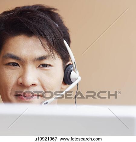 Stock Photo - Close-up of a male customer service representative talking on a headset and using a laptop. Fotosearch
