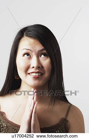 Stock Image - Close-up of a young woman smiling in a prayer position. Fotosearch
