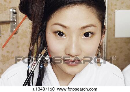 Stock Image - Portrait of a young woman applying make-up on her face. Fotosearch