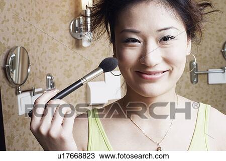 Stock Image - Portrait of a young woman applying make-up on her face. Fotosearch
