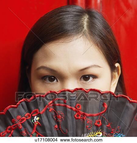 Picture - Portrait of a young woman covering her mouth with a folding fan. Fotosearch