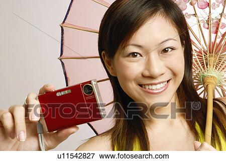 Stock Photo - Portrait of a young woman holding a digital camera and a parasol. Fotosearch