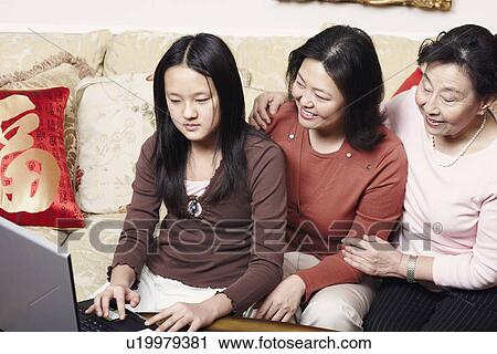 Stock Image - Close-up of a daughter using a laptop with her mother and her grandmother sitting beside her. Fotosearch