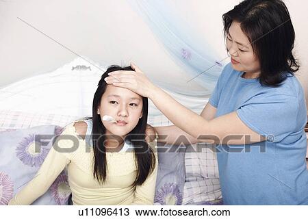 Stock Image - High angle view of a mother's hand on her daughter's forehead. Fotosearch