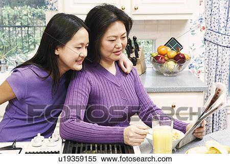 Stock Photography - Side profile of a mother and her daughter reading a newspaper. Fotosearch