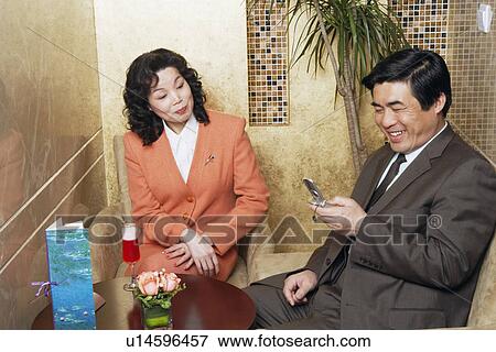 Stock Photo - Businessman sitting with a businesswoman in a restaurant looking at a mobile phone. Fotosearch