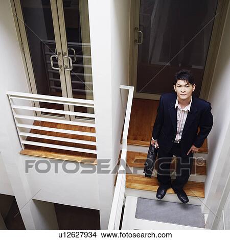 Picture - High angle view of a businessman standing on a staircase and holding a bag. Fotosearch