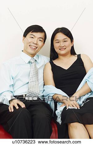 Stock Image - Portrait of a businessman and a mid adult woman sitting together on a couch and smiling. Fotosearch
