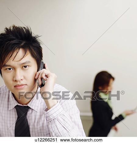 Portrait of a businessman talking on a mobile phone with a businesswoman in the background View Large Photo Image Stock Image - Portrait of a businessman talking on a mobile phone with a businesswoman in the background. Fotosearch