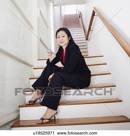 Stock Image - Portrait of a businesswoman sitting on a staircase and holding a mobile phone. Fotosearch