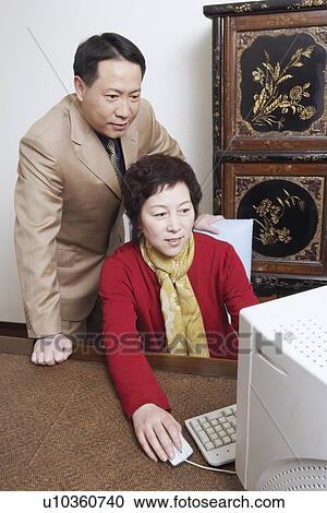 Stock Image - Businesswoman using a computer with a businessman standing behind her. Fotosearch