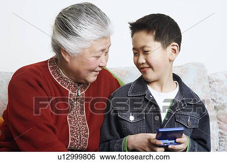 Close-up of a boy sitting with his grandmother holding a video game console View Large Photo Image Stock Photograph - Close-up of a boy sitting with his grandmother holding a video game console. Fotosearch