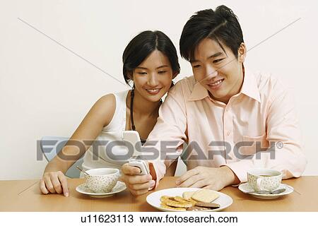 Close-up of a young couple sitting and looking at a mobile phone View Large Photo Image Stock Image - Close-up of a young couple sitting and looking at a mobile phone. Fotosearch