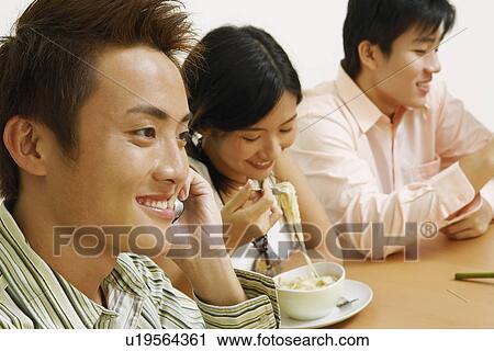 Close-up of a young man talking on a mobile phone with a young couple sitting beside him View Large Photo Image Stock Image - Close-up of a young man talking on a mobile phone with a young couple sitting beside him. Fotosearch