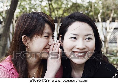 Close-up of a young woman whispering secrets into her friend's ear View Large Photo Image Stock Photo - Close-up of a young woman whispering secrets into her friend's ear. Fotosearch