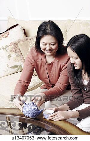 Stock Image - High angle view of a mother pouring tea for her daughter. Fotosearch
