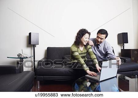 Stock Image - Mature couple sitting on a couch using a laptop. Fotosearch