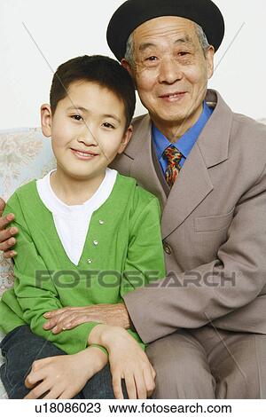 Stock Image - Portrait of a boy sitting on a couch with his grandfather smiling. Fotosearch