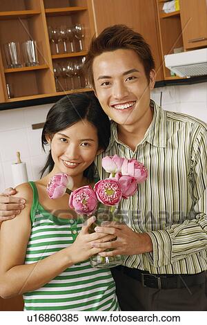Stock Photography - Portrait of a young couple holding a flower vase in the kitchen. Fotosearch