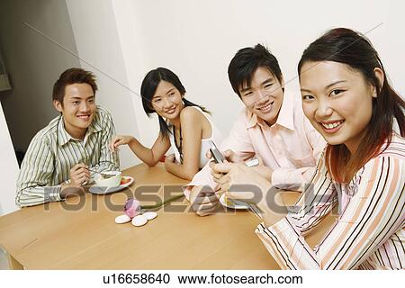 Portrait of a young woman holding a mobile phone and sitting with her friends View Large Photo Image Stock Image - Portrait of a young woman holding a mobile phone and sitting with her friends. Fotosearch
