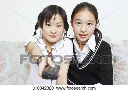 Stock Image - Portrait of a young woman sitting together with her sister holding a remote control. Fotosearch
