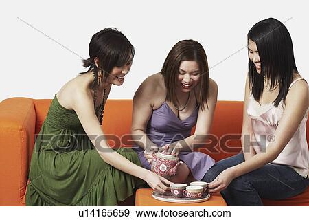 Three young women sitting on a couch with tea cups View Large Photo Image Stock Photo - Three young women sitting on a couch with tea cups. Fotosearch