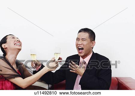 Stock Image - Close-up of a businessman and a mid adult woman holding glasses of champagne and laughing together. Fotosearch