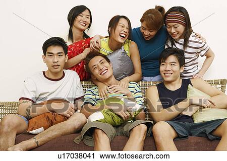 Close-up of three young men sitting on a couch with four women standing behind them View Large Photo Image Stock Image - Close-up of three young men sitting on a couch with four women standing behind them. Fotosearch
