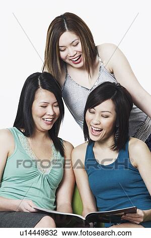 Stock Image - Close-up of three young women looking at a magazine. Fotosearch
