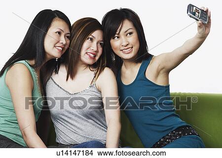 Picture - Close-up of three young women taking a photograph of themselves with a mobile phone camera. Fotosearch