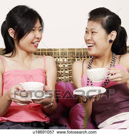Close-up of two young women holding tea cups on a couch and smiling View Large Photo Image Stock Photo - Close-up of two young women holding tea cups on a couch and smiling. Fotosearch