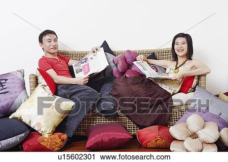 Stock Image - Portrait of a mid adult man and a young woman reclining on a couch and smiling. Fotosearch