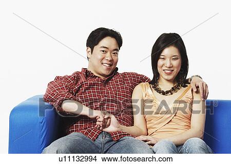 Portrait of a young couple sitting on a couch holding hands View Large Photo Image Picture - Portrait of a young couple sitting on a couch holding hands. Fotosearch