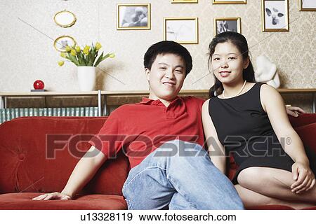 Stock Photo - Portrait of a young couple sitting on a couch smiling. Fotosearch